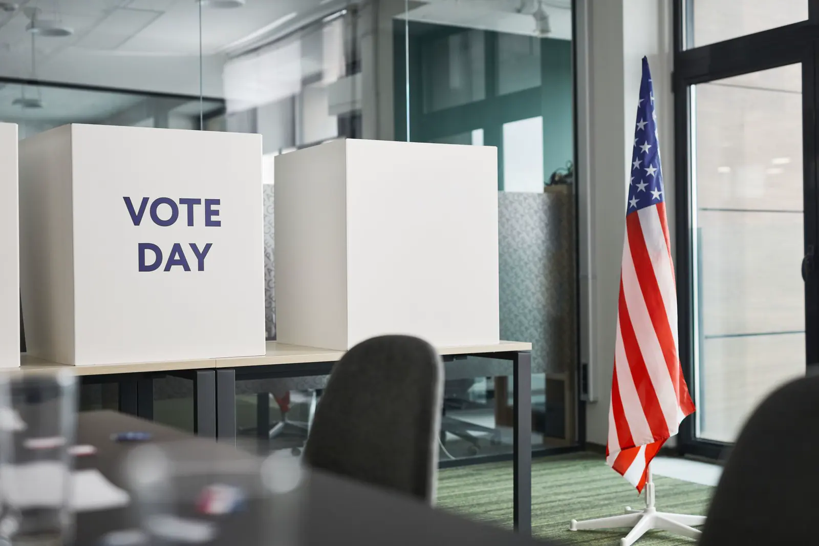 A row of empty voting booths in a room, with an American flag standing beside them.