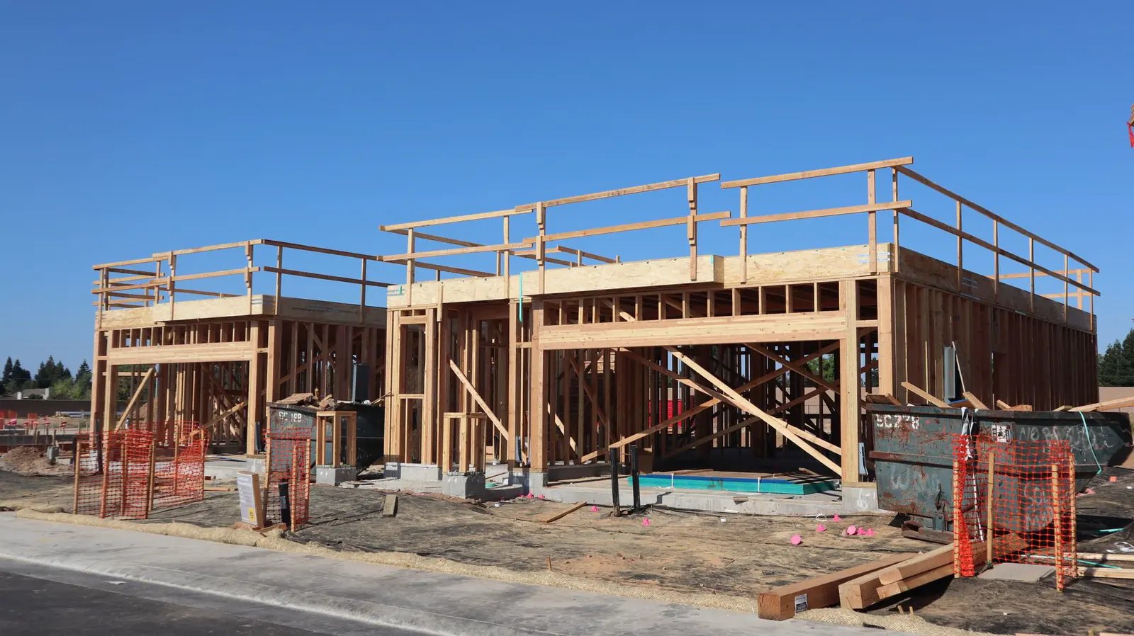 Wooden frames of new houses under construction, with stacks of lumber in the foreground.